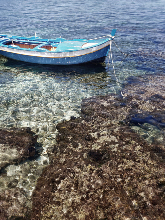 a boat floating in the Sicilian shore, volcanic rocks and crystal clear water